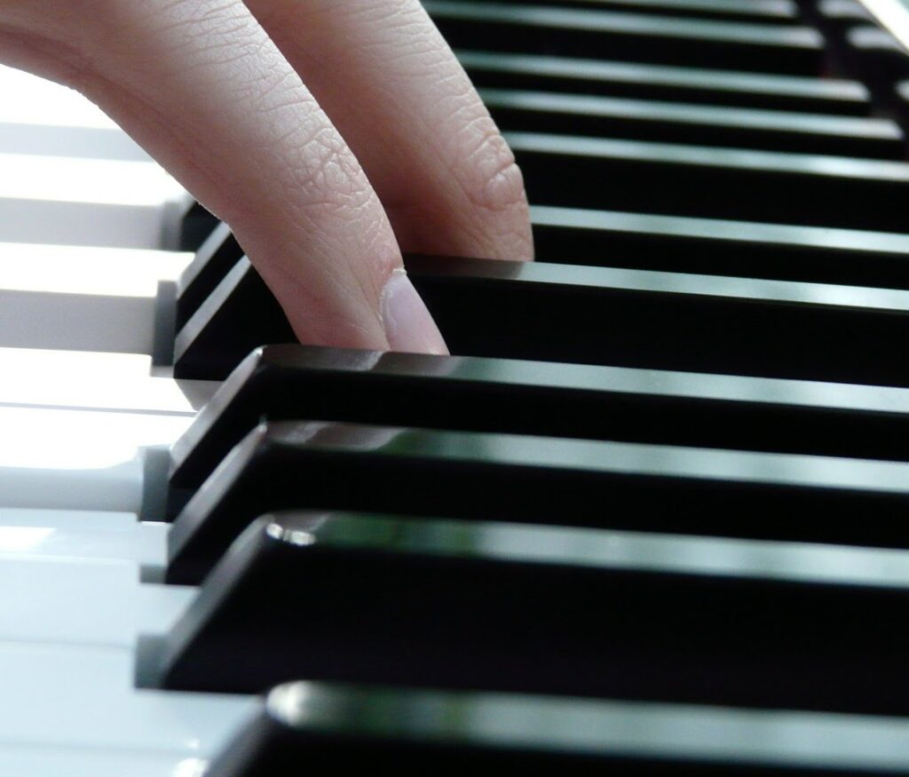 A close-up of a piano. Two fingers can be seen pressing on keys.